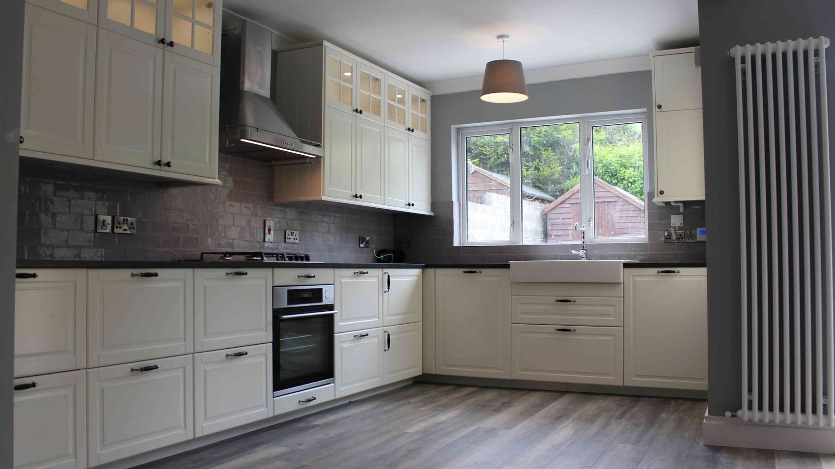 A white shaker kitchen with a grey splashback, wall cabinets and a column radiator