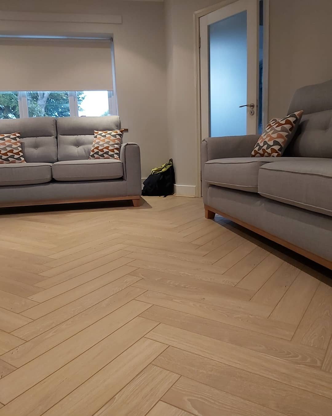 A living room with a herringbone floor and two grey sofas