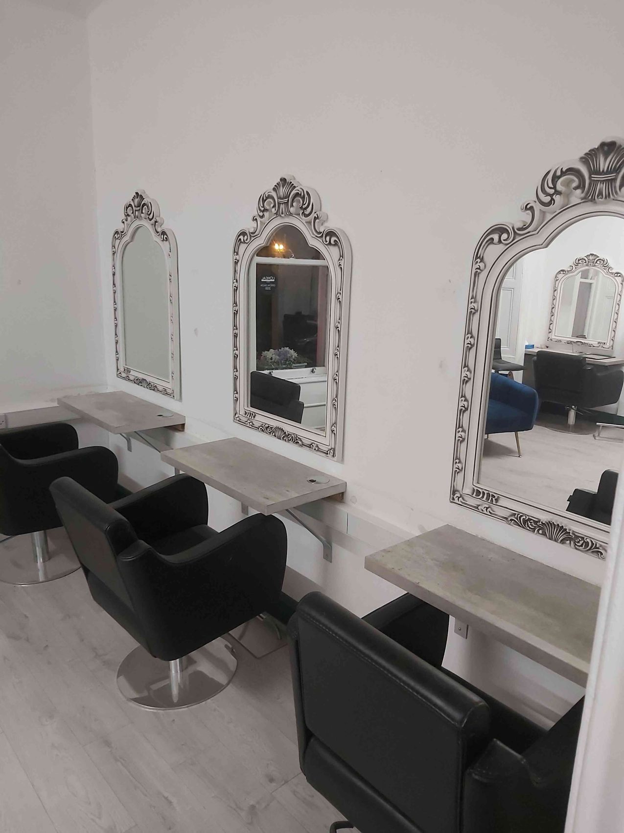 A salon with ornate mirrors over long counters and black styling chairs