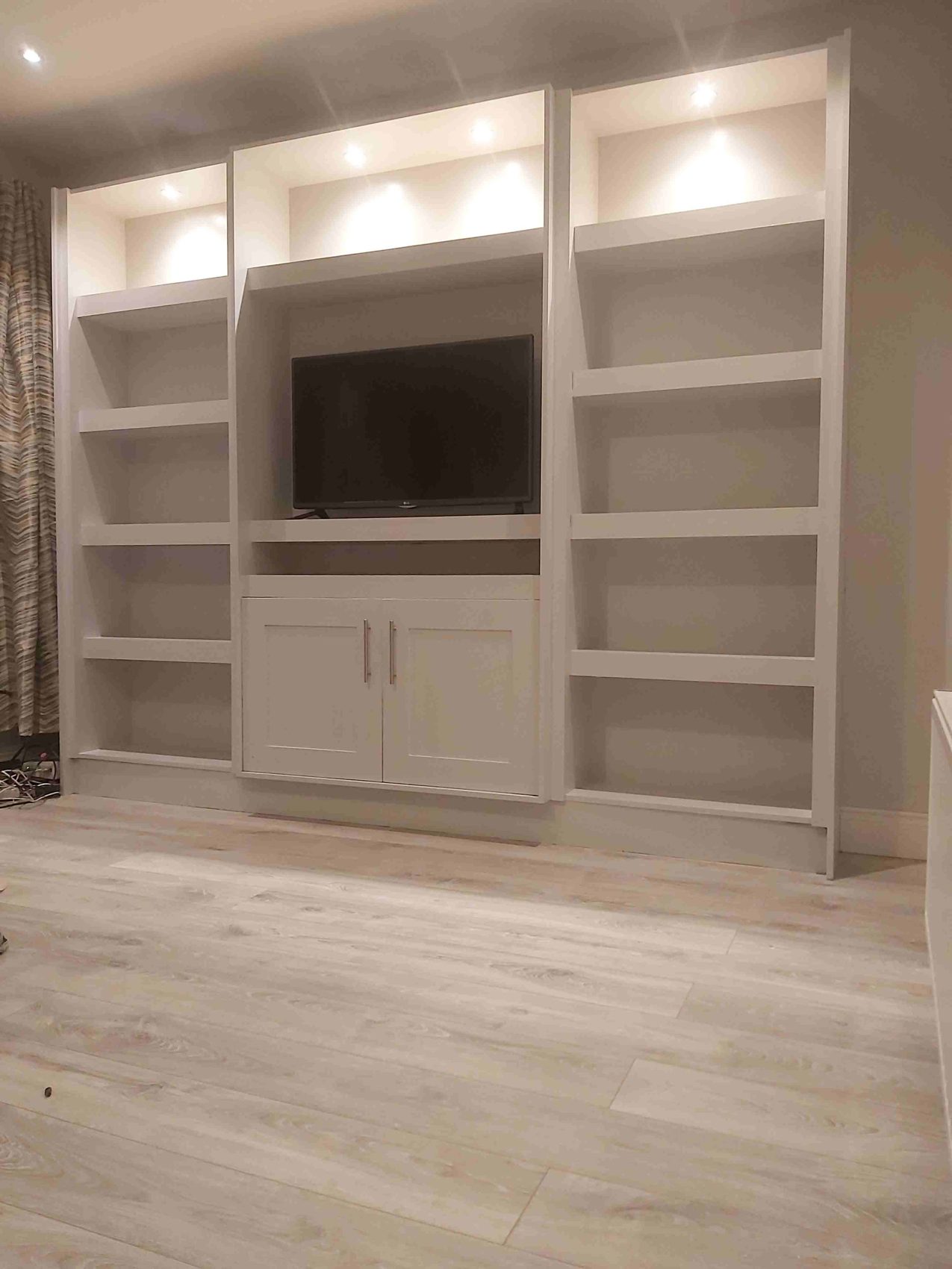 Built-in white shelving and a TV unit with lit alcoves